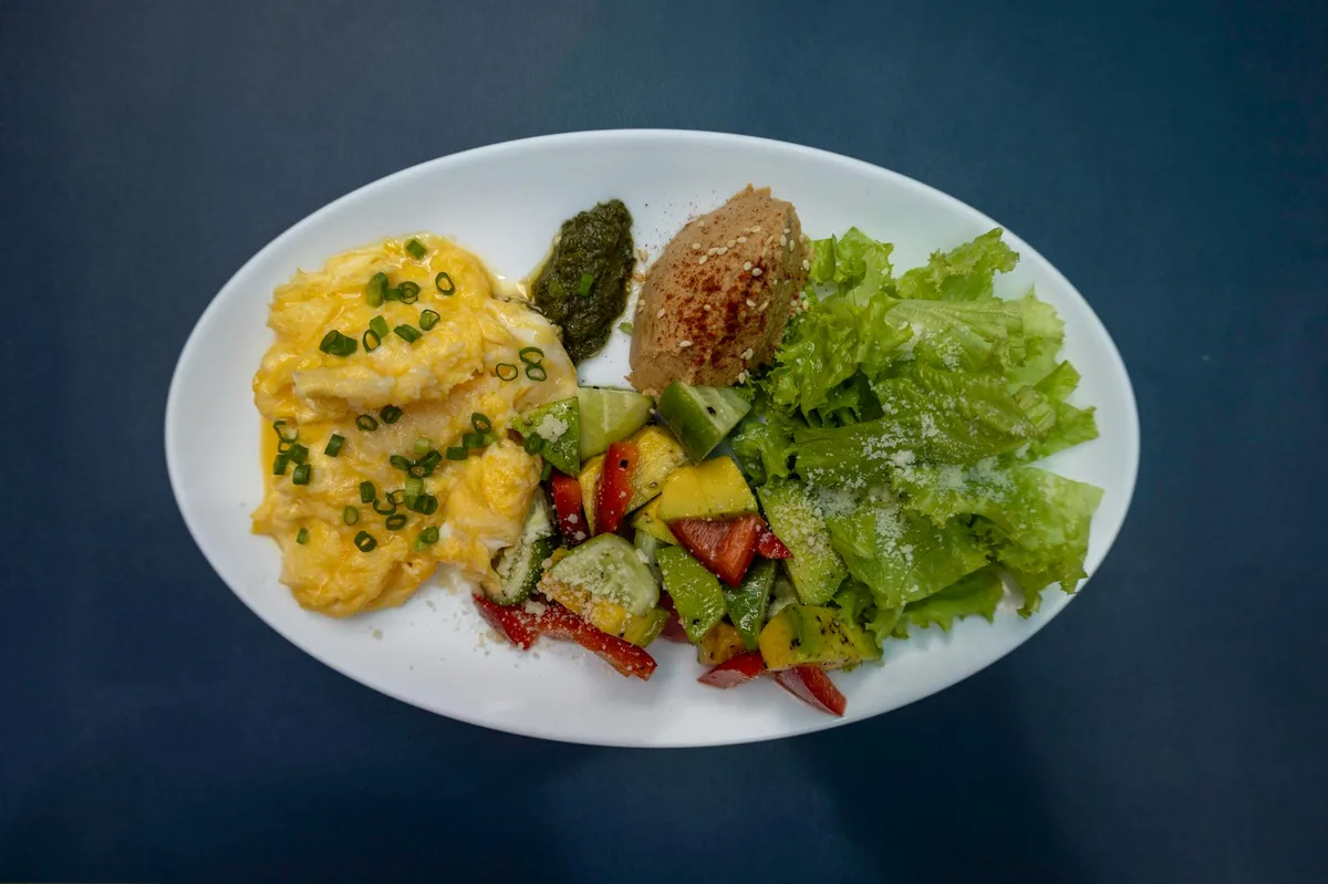 Scrambled eggs, fresh salad, and greens on a white plate for a hearty meal.